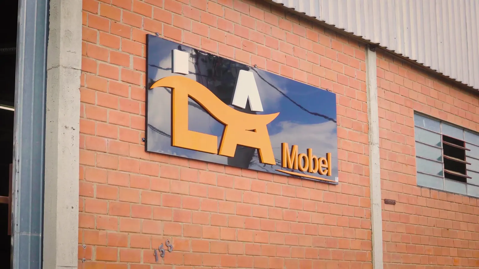 Fachada da fábrica da La Mobel, com o logo na parede de tijolos