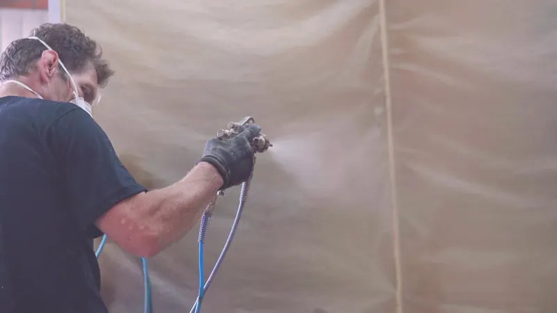 Verniz sendo aplicado com pistola na cabine de pintura