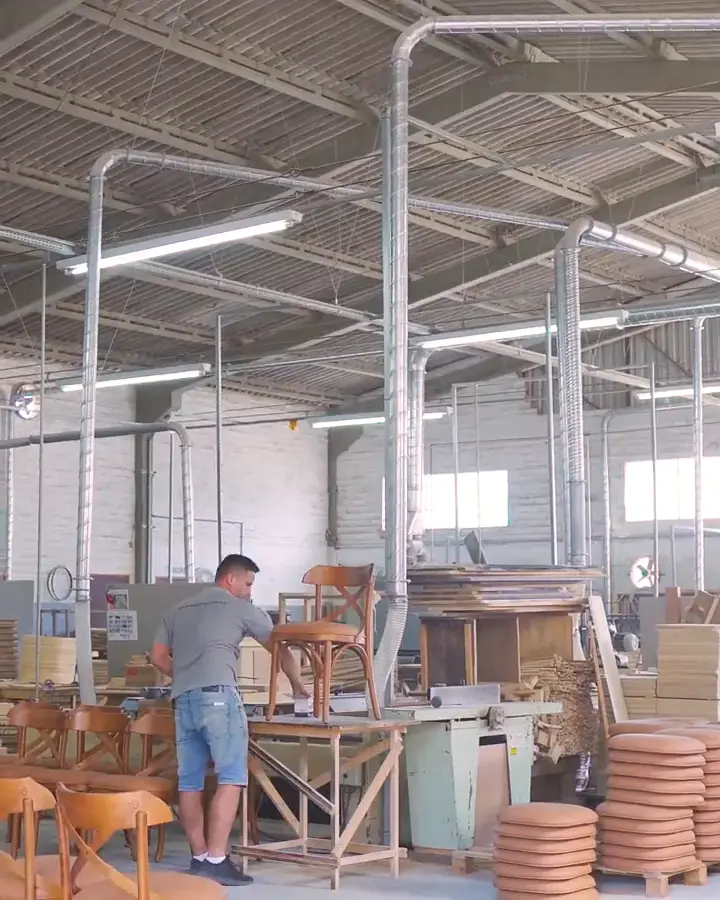 O galpão da fábrica e um funcionário montando uma Cadeira X estofada na bancada
